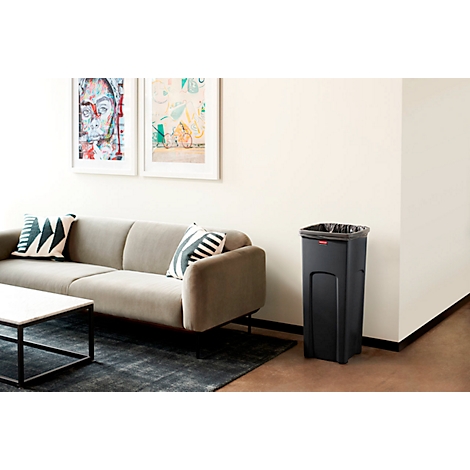 Schwarzer Mülleimer in Wohnzimmer. Sofa, Teppich, Bilder, und Couchtisch im Hintergrund.