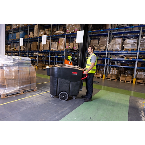 Een man in een magazijn duwt een zwarte transportwagen. Rechts staat een vorkheftruck, op de achtergrond staan opslagrekken.