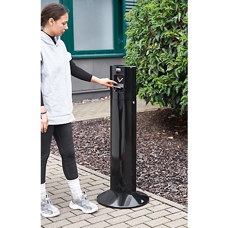 Junge Frau wirft etwas in eine schwarze Mülltonne. Sie trägt eine graue Kapuzenjacke und schwarze Hose.