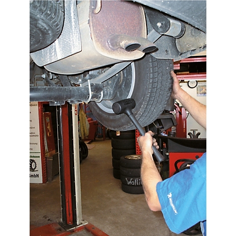 Ein Mechaniker schlägt mit einem Gummihammer auf einen Reifen, der an einem angehobenen Auto befestigt ist.