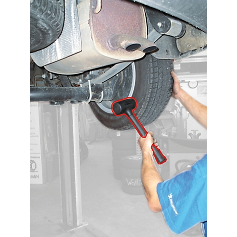 Ein Mann schlägt mit einem Hammer auf einen Reifen an einem Auto.