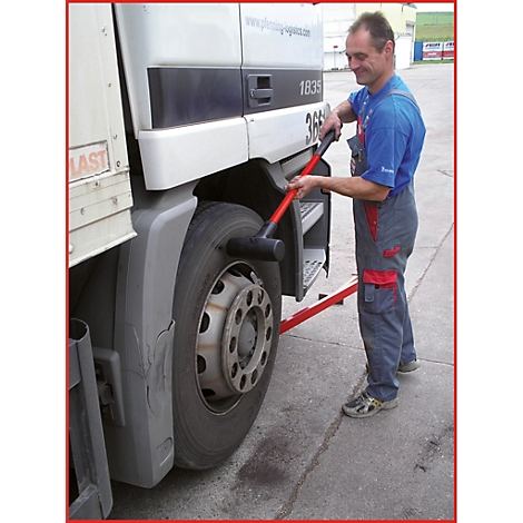 Ein Mann schlägt mit einem Hammer auf einen LKW-Reifen. Der Reifen steht auf einer roten Plattform.