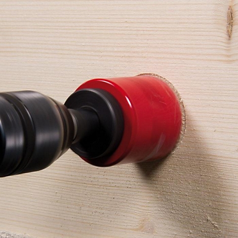 Een rode gatzagen boort een gat in een houten plank. De boor is in beweging.