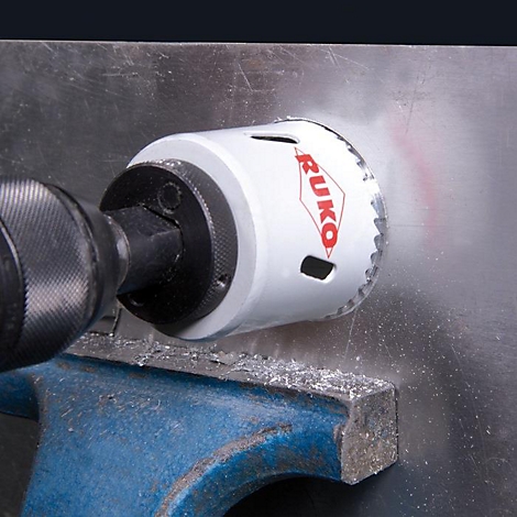 Een witte gatenzaag met rode "RUKO" belettering zaagt een gat in een metalen plaat. Vonken vliegen rond.