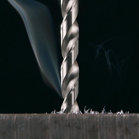 Close-up van een boor die in metaal boort. Rook stijgt op. De achtergrond is zwart.