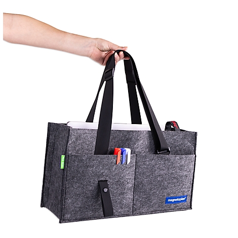 Une main porte un sac en feutre gris avec des bretelles noires et des stylos dans la poche avant.