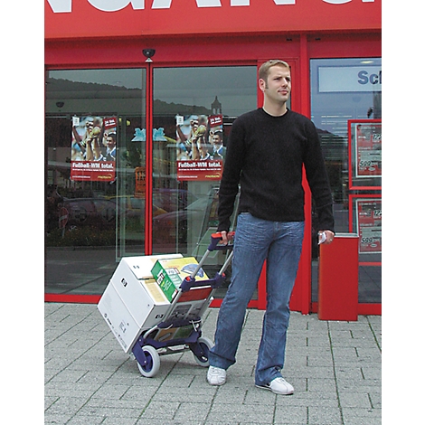 Man pulls a shopping cart with boxes in front of a store. Red lettering, glass door.