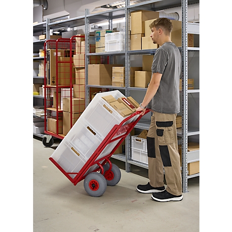 Ein Mann schiebt einen roten Transportwagen mit Boxen durch ein Lager.