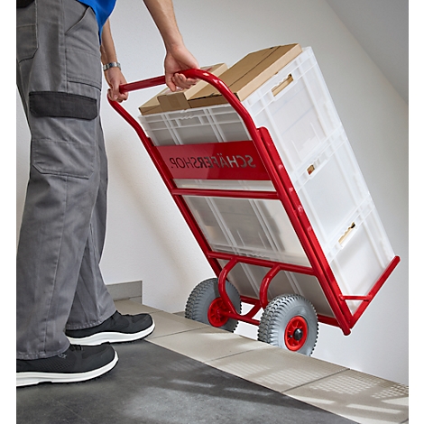 Person zieht eine rote Sackkarre mit Kisten und Kartons die Treppe hoch. Auf der Sackkarre steht "SCHWERER SHOP".