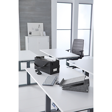 Un bureau avec des accessoires, tels qu'un clavier, une souris et un sac. En arrière-plan, des fenêtres et une chaise de bureau. Ambiance lumineuse et moderne.