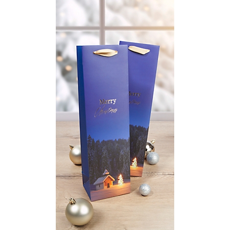 Deux sacs cadeaux de Noël bleus avec imprimé paysage et poignées dorées sont posés sur une table en bois. La neige scintille en arrière-plan.