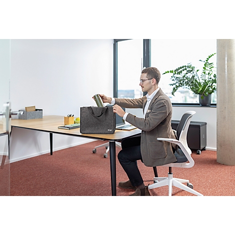 Un homme dans un bureau s'assoit et sort quelque chose d'un sac gris sur le bureau.