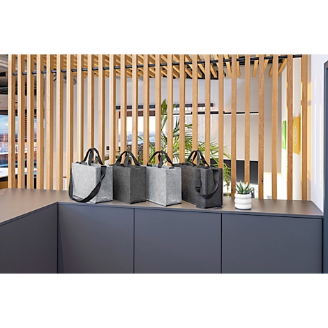 Sacs en feutre gris posés sur une étagère grise devant un mur à lattes en bois. Il y a une petite plante en pot sur l'étagère.