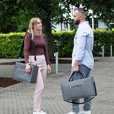 Deux personnes avec des sacs d'ordinateur portables gris discutent. Une femme porte un sac sur son épaule, l'homme dans sa main.