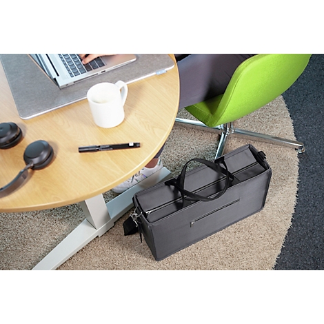 Sac noir au sol, table avec ordinateur portable, tasse à café, écouteurs. Personne assise sur une chaise verte.