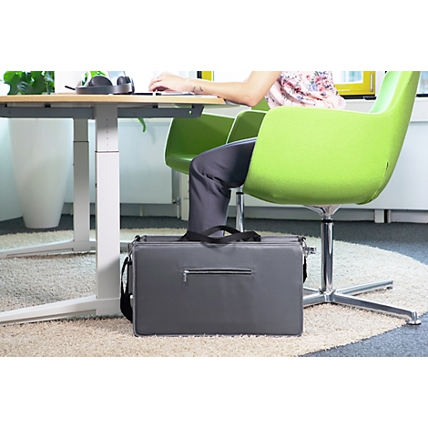 Personne au bureau avec un ordinateur portable et une chaise verte. Sac gris utilisé comme repose-pieds.