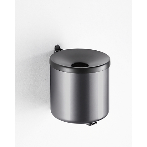 Gray, wall-mounted trash can. The lid has a hole, below is a black ring. On a white background.