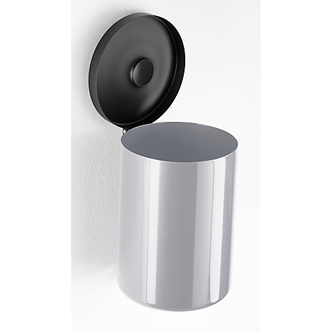 Gray cylindrical trash can with open black lid on a white wall.