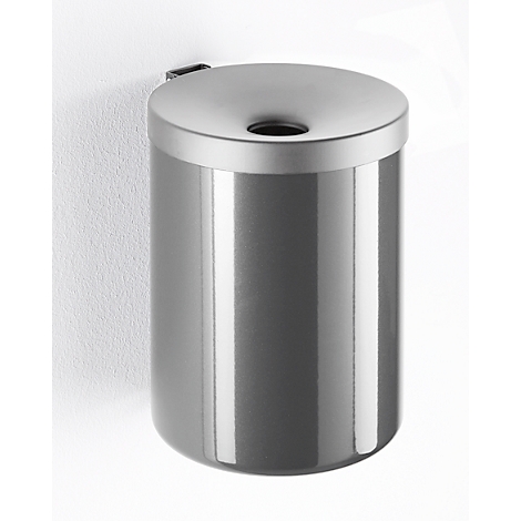 Gray, cylindrical wall-mounted waste bin with lid. Top with hole for trash. Mounted on white wall.