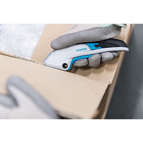 A gloved hand cutting open a cardboard box with a cutter. The cutter has a blue accent and the writing martor.