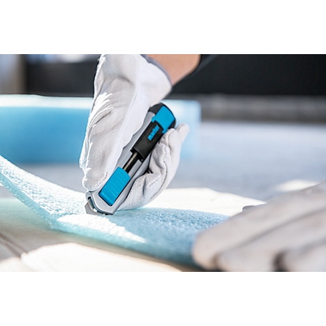 Person cuts blue foam material with a utility knife, gloves protect the hands.