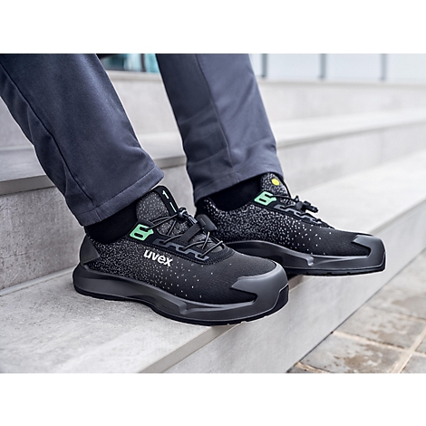 Black Uvex safety shoes on feet, sitting on a staircase.