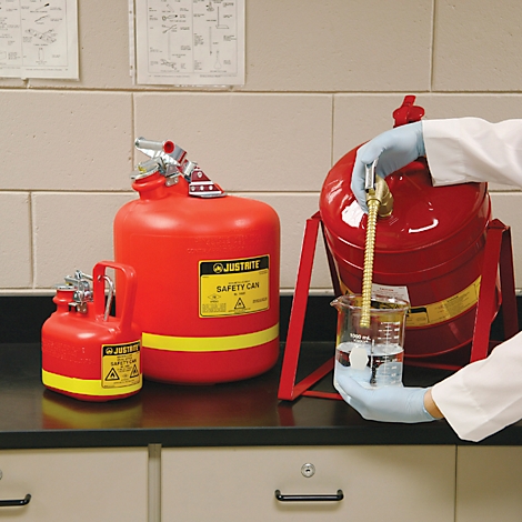 Red safety cans in a laboratory. A scientist in gloves is filling a beaker.