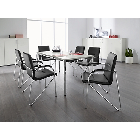 A conference table with black chairs in a bright room. Paper and a carafe are on the table.