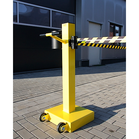 Barrière mobile jaune avec ruban d'avertissement noir et jaune ; se dresse sur des pavés.