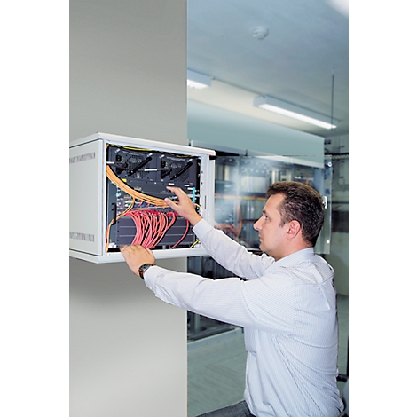 A man works on a server cabinet. He connects red and yellow cables. The cabinet is mounted in a wall.