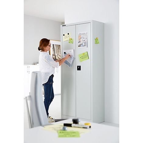Une femme en jean et chemisier blanc fixe des notes sur une armoire blanche. Sur les notes, on peut lire "idées".