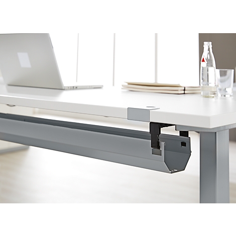 Bureau blanc avec ordinateur portable, bouteille d'eau, verres et passe-câbles gris.