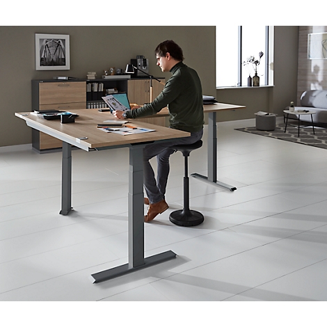 Man at height-adjustable desk, looking at laptop. Ergonomic work in modern office.