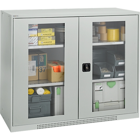 Armario gris con puertas de cristal, lleno de herramientas, cajas de herramientas y materiales. Manija de puerta negra en el medio.