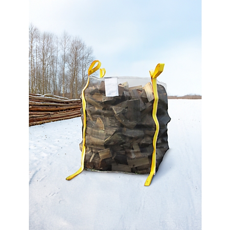 Ein Sack mit Kaminholz, der auf Schnee vor einem Waldhintergrund steht. Gelbe Gurte halten den Sack zusammen.