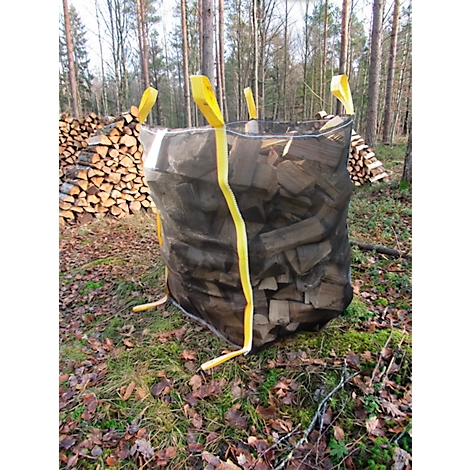Ein großer, mit Holz gefüllter Sack steht in einem Waldstück. Gelbe Schlaufen sind am Sack befestigt. Im Hintergrund sind weitere Holzstapel zu sehen.