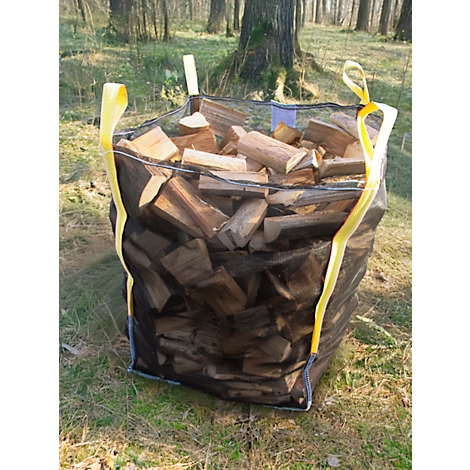 Ein großer, mit Brennholz gefüllter schwarzer Sack mit gelben Schlaufen, steht im Wald.