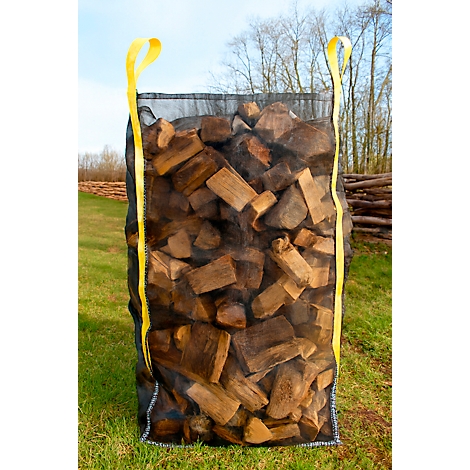 Schwarze Netztasche mit Kaminholz auf grüner Wiese. Gelbe Schlaufen oben.