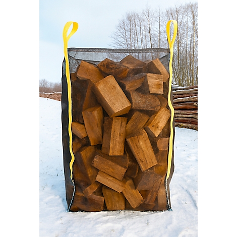 Ein großer schwarzer Sack, gefüllt mit Holzbriketts, steht im Schnee. Gelbe Tragegurte ragen heraus.
