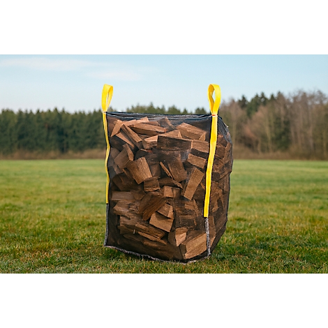 Ein großer, mit Holzscheiten gefüllter Sack steht auf einer Wiese. Gelbe Schlaufen dienen als Tragegriffe.