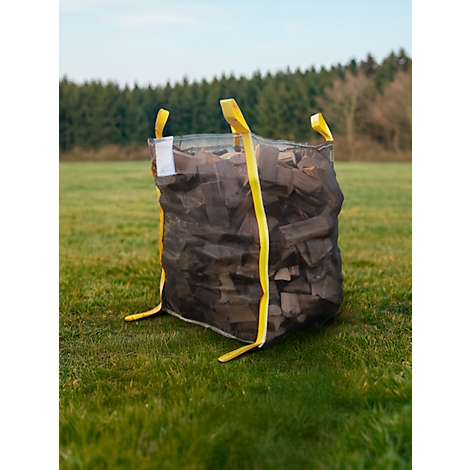 Un grand sac rempli de bûches se dresse dans une prairie verte. Le sac est marron foncé, avec des sangles jaunes et se trouve devant une forêt.