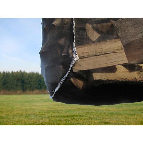 Un grand sac rempli de bois, sur fond de champ vert et de forêt. Le bois est visible à travers un filet noir.