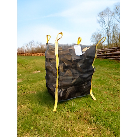 Un grand sac noir rempli de bûches est posé sur une prairie. Des boucles jaunes sont attachées au sac. Dans le ciel, ciel bleu avec des nuages.