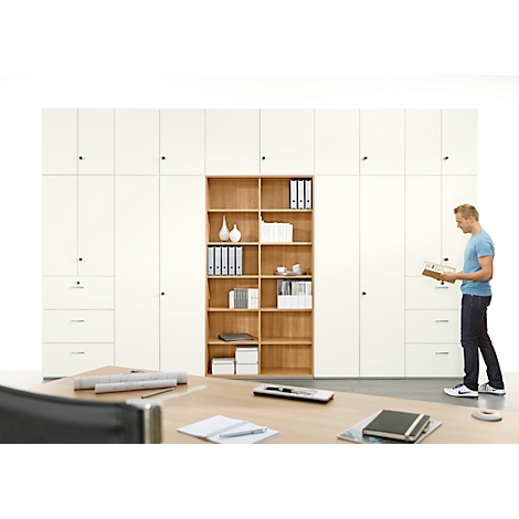 A man reads in an office in front of a cabinet. Documents and a notebook lie on the table.
