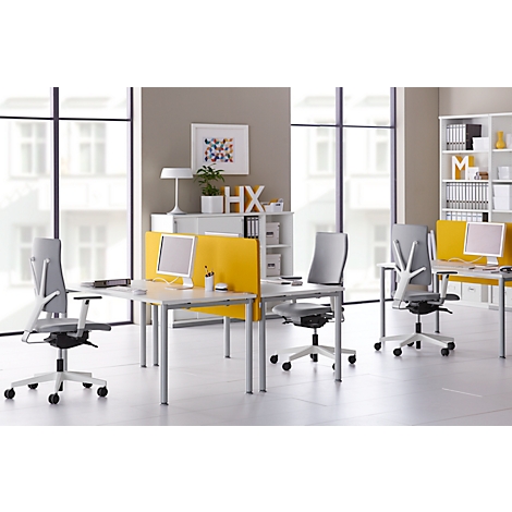 Kantoor met witte bureaus, grijze stoelen en gele schotten. Witte planken met decoratie, ramen op de achtergrond.