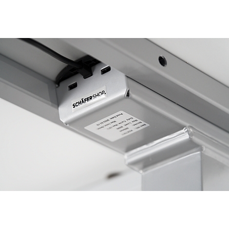 Close-up van de onderkant van een tafel. Op een metalen plaat staat 'SCHÄFER SHOP'. Kabels en een sticker zijn zichtbaar.