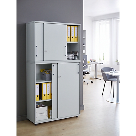 Grey filing cabinet with sliding doors, filled with files and office accessories. Office in the background.