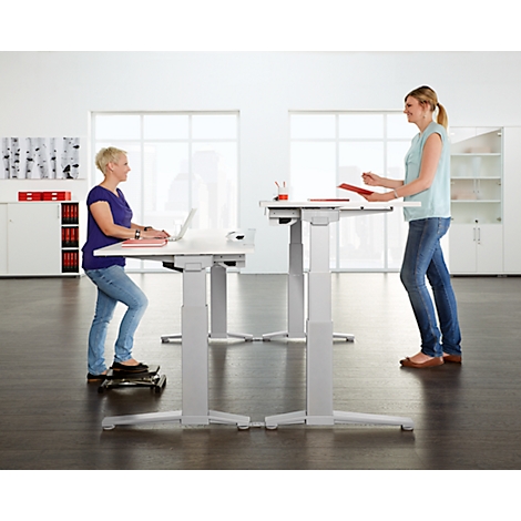 Two women standing and working at height-adjustable desks in a bright office.