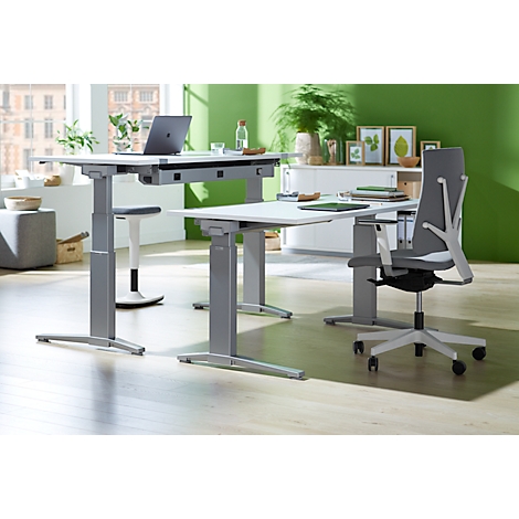 Two height-adjustable desks in a modern office. A laptop sits on the table. Ergonomic office chair.