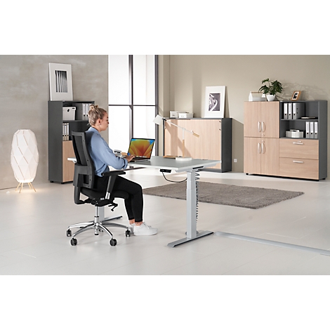 Woman sitting at height-adjustable desk working on laptop. Office furniture with cabinets.